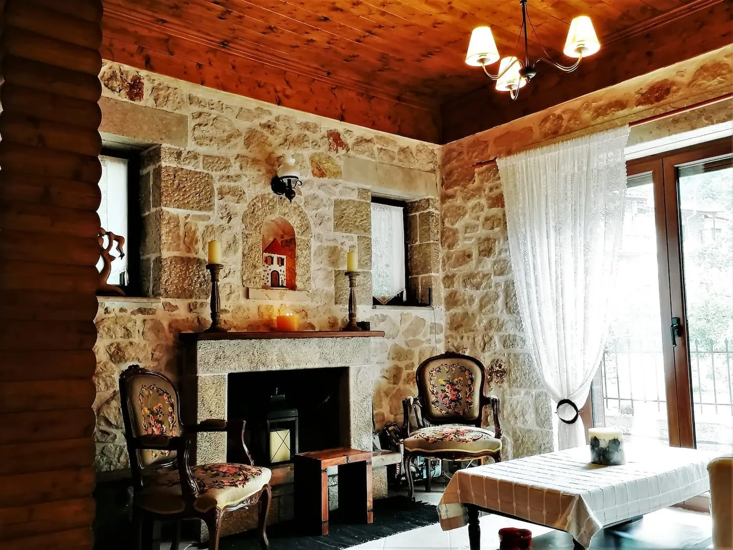Σαλόνι με πέτρινους τοίχους, πέτρινο τζάκι, πολυθρόνες και ξύλινο ταβάνι