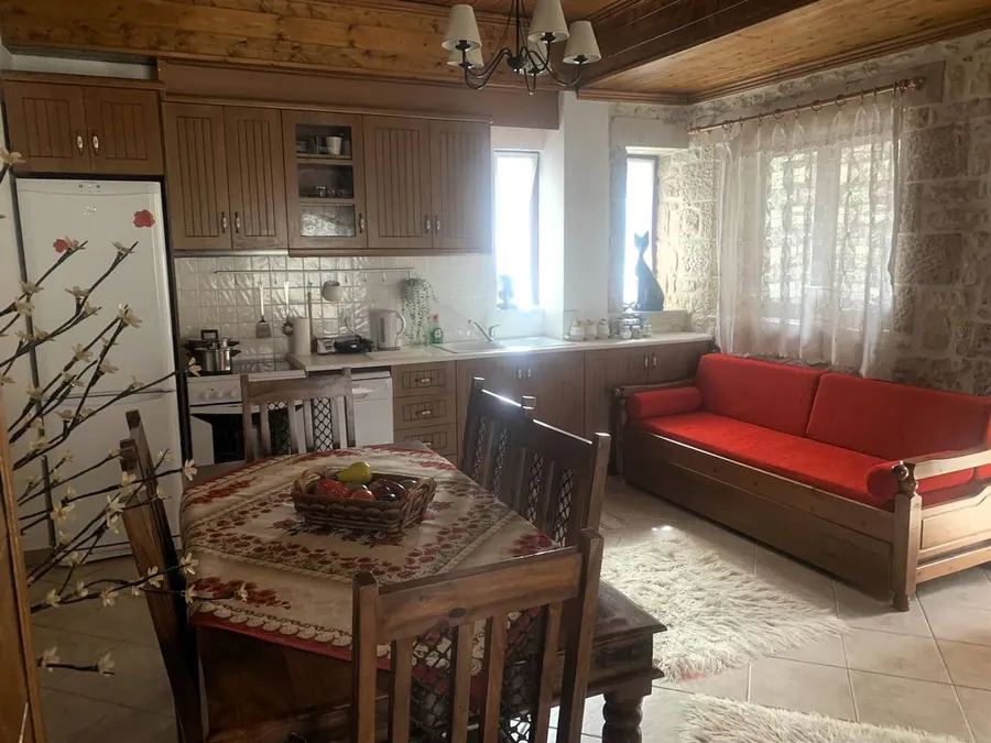 Τραπεζαρία με κεντημένο τραπεζομάντιλο, κόκκινος καναπές και η κουζίνα